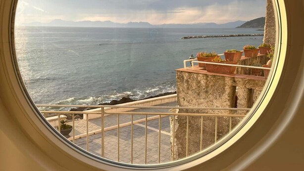 Uma janela redonda com vista para o mar e um edifício de pedra.