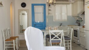 Una cocina compacta con electrodomésticos blancos, una puerta azul y una zona de comedor con sillas y mesa blancos.