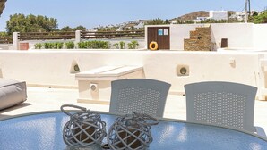 Un espacio al aire libre iluminado por el sol con mesa y sillas, una piscina pequeña y vistas a un pueblo costero.