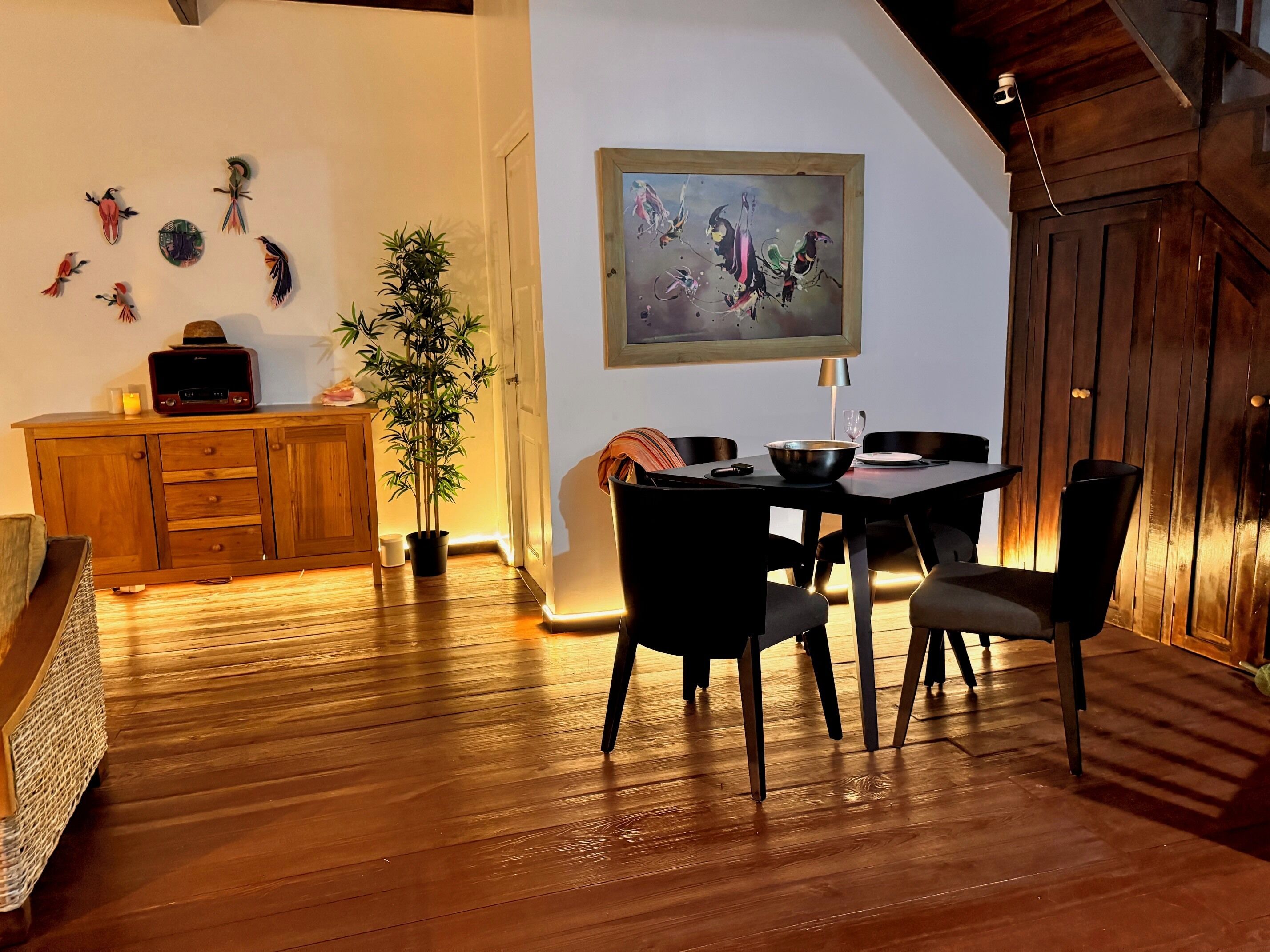 A dining area with a wooden table and chairs, a potted plant, and a painting on the wall.