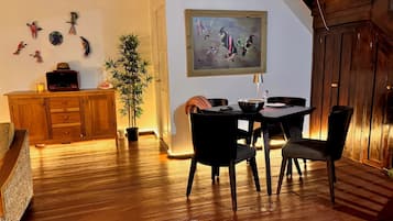 A dining area with a wooden table and chairs, a potted plant, and a painting on the wall.