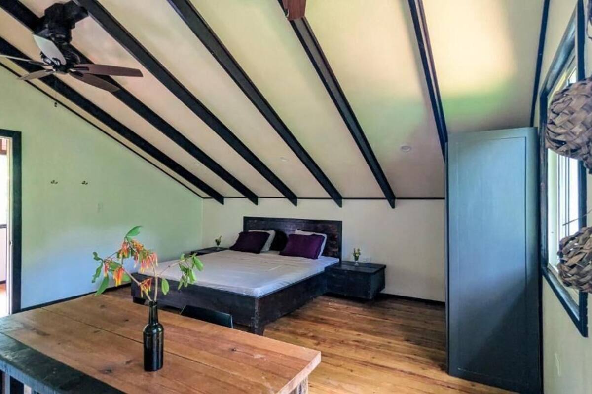 A bedroom with a sloped ceiling, a bed, a bedside table, a nightstand, and a window.