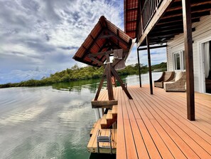 Una terraza de madera con vista a un cuerpo de agua tranquilo y abundante vegetación al fondo.