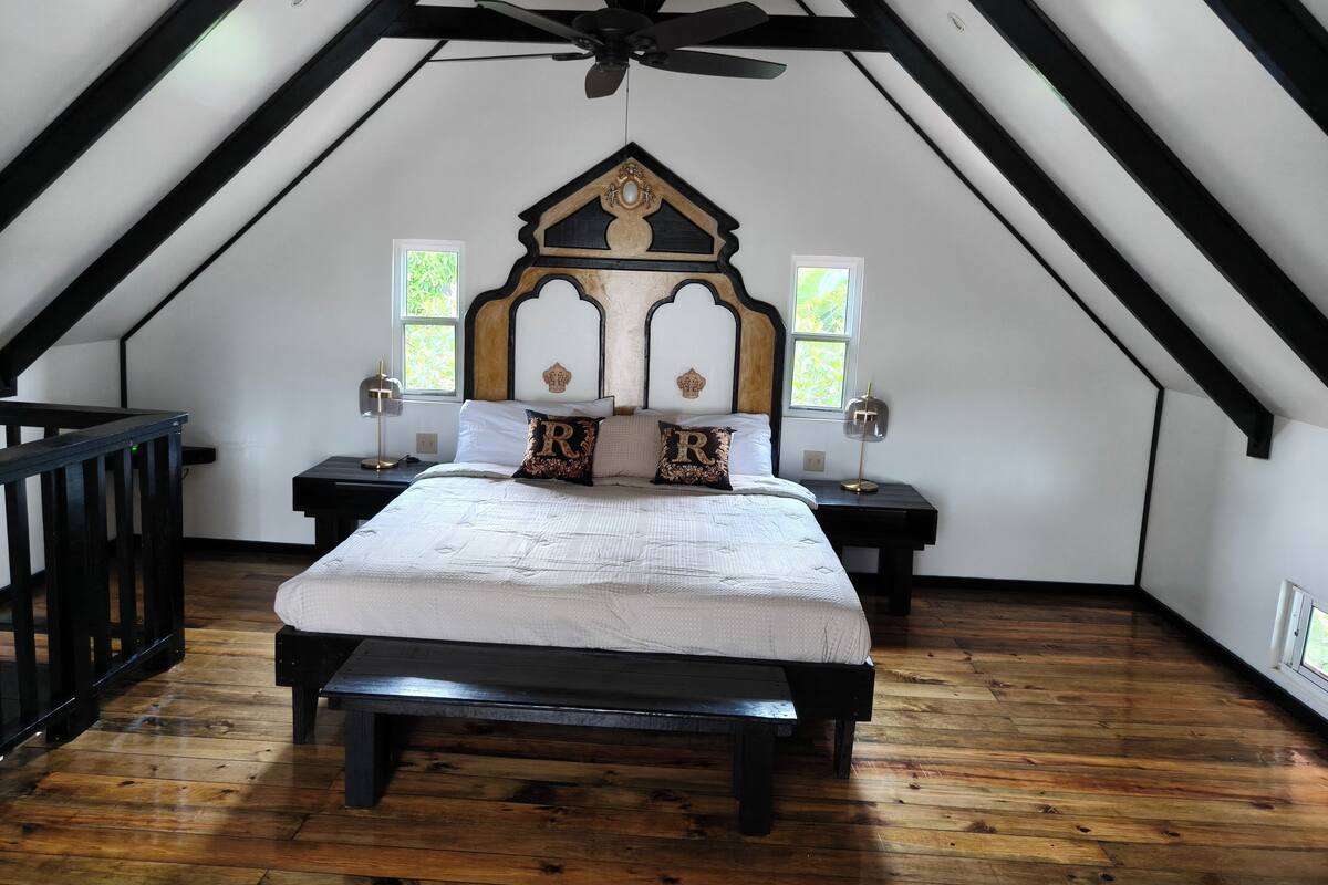 A bedroom with a sloped ceiling, a wooden bed frame, two bedside tables, and a bench.
