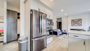 A modern kitchen with stainless steel appliances, a grey trash bin, and a white countertop.