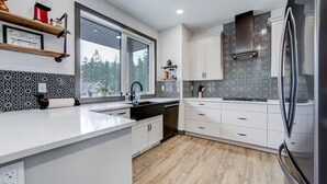 A modern kitchen with white cabinetry, a large window, and a stainless steel refrigerator.