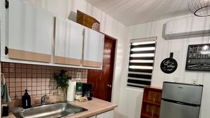 Uma cozinha compacta com armários brancos, pia de aço inoxidável, máquina de café e geladeira.