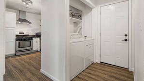 Eine moderne Küche mit weißen Schränken, einem Edelstahlbackofen und einer Mikrowelle. Der Boden ist aus Holz und es gibt eine weiße Tür mit Griff.