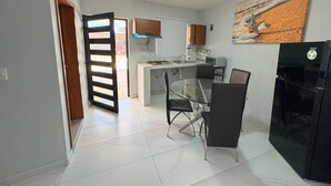 A compact kitchen with a dining area, featuring a glass table and chairs, a refrigerator, and a microwave. - Residencia Gran Coyula Orange 502 (Tonala)