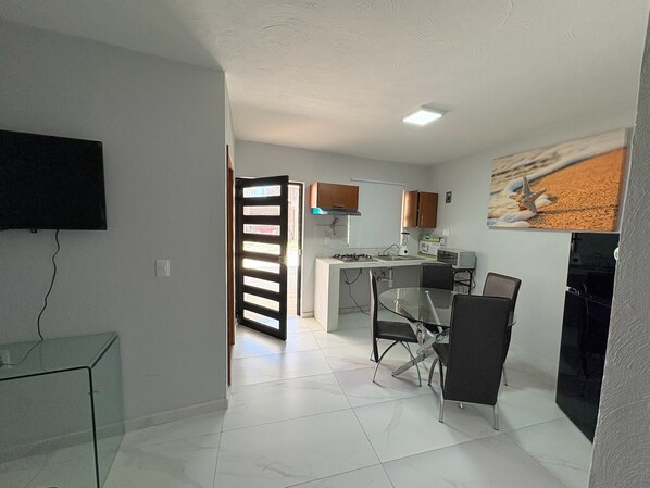 A modern kitchen with a central island, a dining area with a glass table, and a TV mounted on the wall. - Residencia Gran Coyula Orange 502 (Tonala)