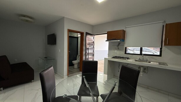 A compact kitchen with a glass dining table, a built-in stove, and a window overlooking a street. - Residencia Gran Coyula Orange 502 (Tonala)