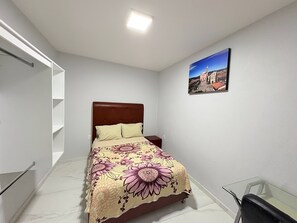 A bedroom with a bed, a nightstand, a glass table, and a painting on the wall. - Residencia Gran Coyula Orange 502 (Tonala)