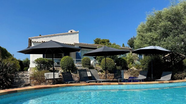A swimming pool with lounge chairs and umbrellas, surrounded by greenery and a building with a white facade. - VILLA LE CLOS BUCCI WITH PRIVATE POOL AND SUPERB SEA VIEW LES HAUTS DE GRIMAUD (Grimaud)