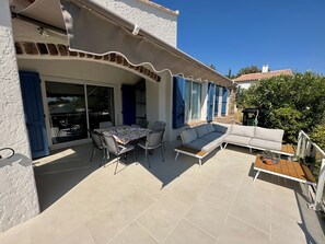 Eine Terrasse mit Tisch, Stühlen und einer Sitzecke, sowie eine Glastür.
