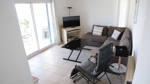 A living room with a sofa, a TV on a stand, a chair, a small table, and a sliding glass door leading to an outdoor area. - VILLA LE CLOS BUCCI WITH PRIVATE POOL AND SUPERB SEA VIEW LES HAUTS DE GRIMAUD (Grimaud)
