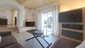 A living room with a sofa, a glass-top coffee table, a fireplace, a TV mounted on the wall, and a sliding glass door leading to an outdoor area. - VILLA LE CLOS BUCCI WITH PRIVATE POOL AND SUPERB SEA VIEW LES HAUTS DE GRIMAUD (Grimaud)