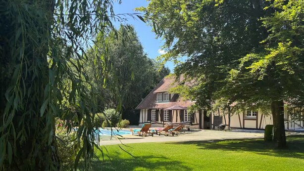 Una casa con piscina, rodeada de césped cuidado y árboles.