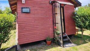 Une petite cabane en bois rouge, dotée d’une petite fenêtre et d’une porte, entourée de verdure.