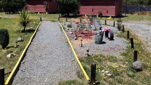 Une grange rouge avec un toit en métal, entourée d’un chemin de gravier et de petites plantes.