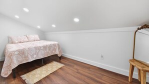 Ein Schlafzimmer mit einem Bett, Holzboden, einem kleinen Hocker und einer Deckenleuchte.