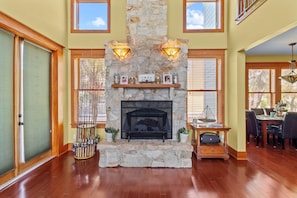 A spacious living room with a stone fireplace, wooden flooring, and large windows. - Magnolia Breeze Getaway - Steinhatchee Florida (Steinhatchee)