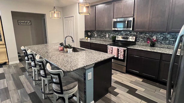 A modern kitchen with a large island, dark wood cabinets, a stainless steel refrigerator, and a microwave. - Perfect 4-bedroom house with AC in peaceful Port Charlotte (Port Charlotte)