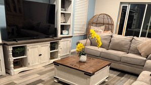 A living room with a TV, wooden cabinet, sofa, and a coffee table with flowers. - Perfect 4-bedroom house with AC in peaceful Port Charlotte (Port Charlotte)