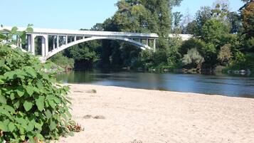 Een witte, gebogen brug over een rivier, omringd door dichte bomen en weelderige begroeiing.