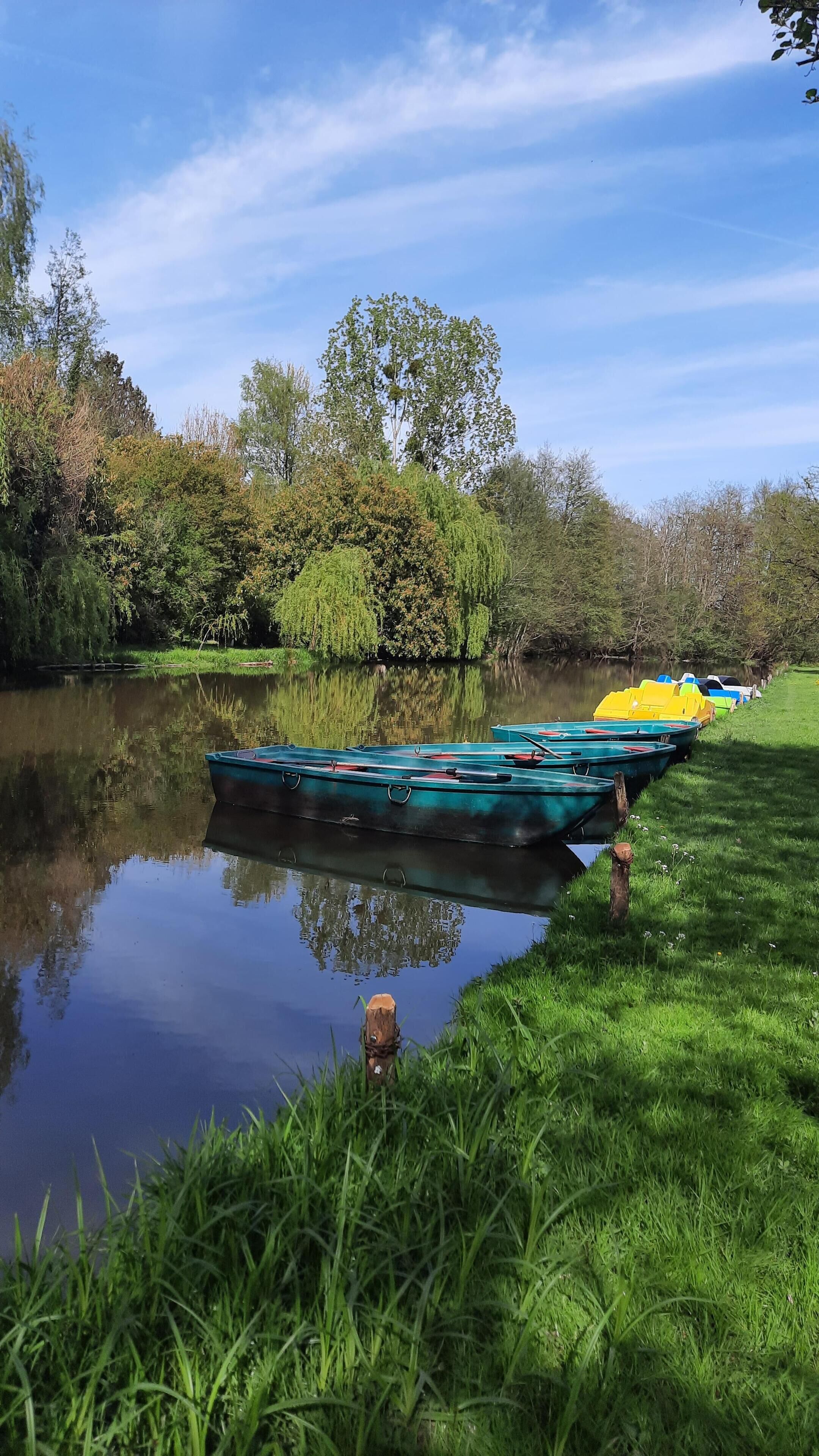 A calm river with boats docked along the grassy bank.