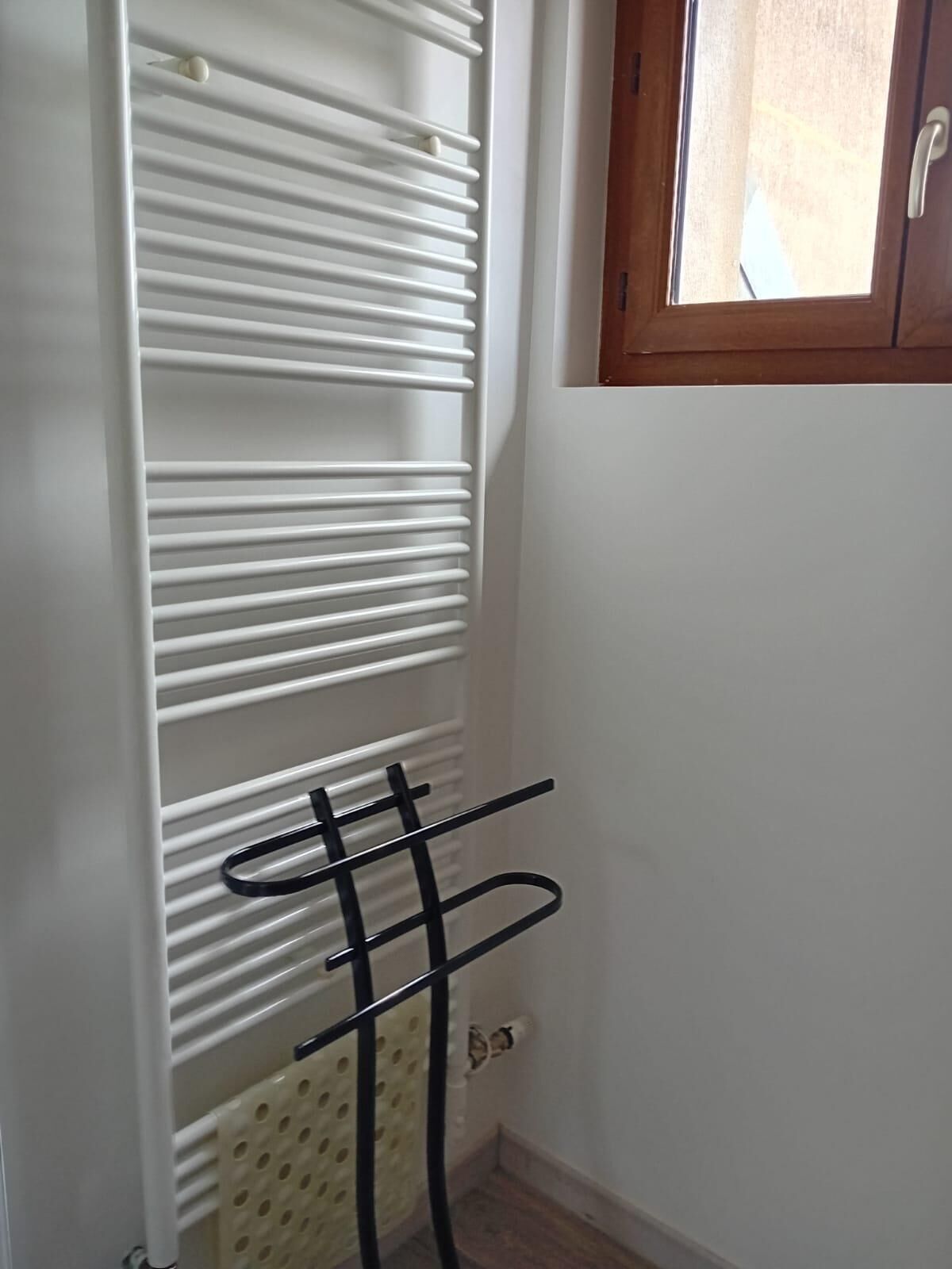 Un radiador blanco con listones horizontales, un estante de metal negro y un ventanal con marco de madera.