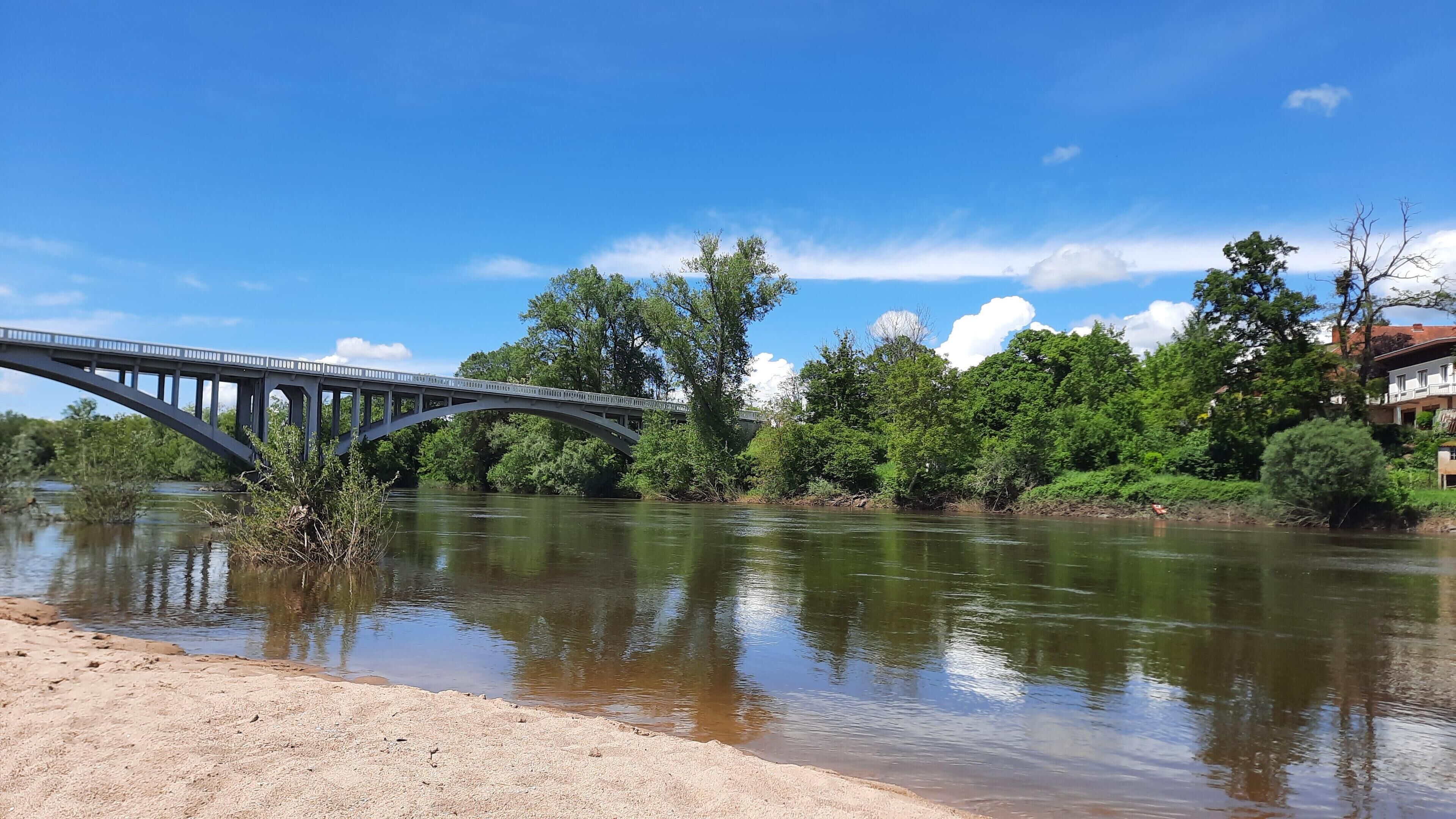 Ein Fluss mit einer Brücke, umgeben von Grünflächen und Gebäuden.
