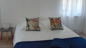 Un dormitorio con cama, dos almohadas, una mesita de noche y una lámpara.