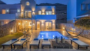 Et moderne hus med to etager, swimmingpool, udendørs møbler og en stenvæg.