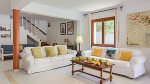 Sala de estar com dois sofás brancos, uma mesa de centro de madeira e uma escada que dá acesso a outro andar.