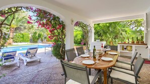 Uma área de refeições ao ar livre com piscina, cadeiras e uma mesa posta para dois.