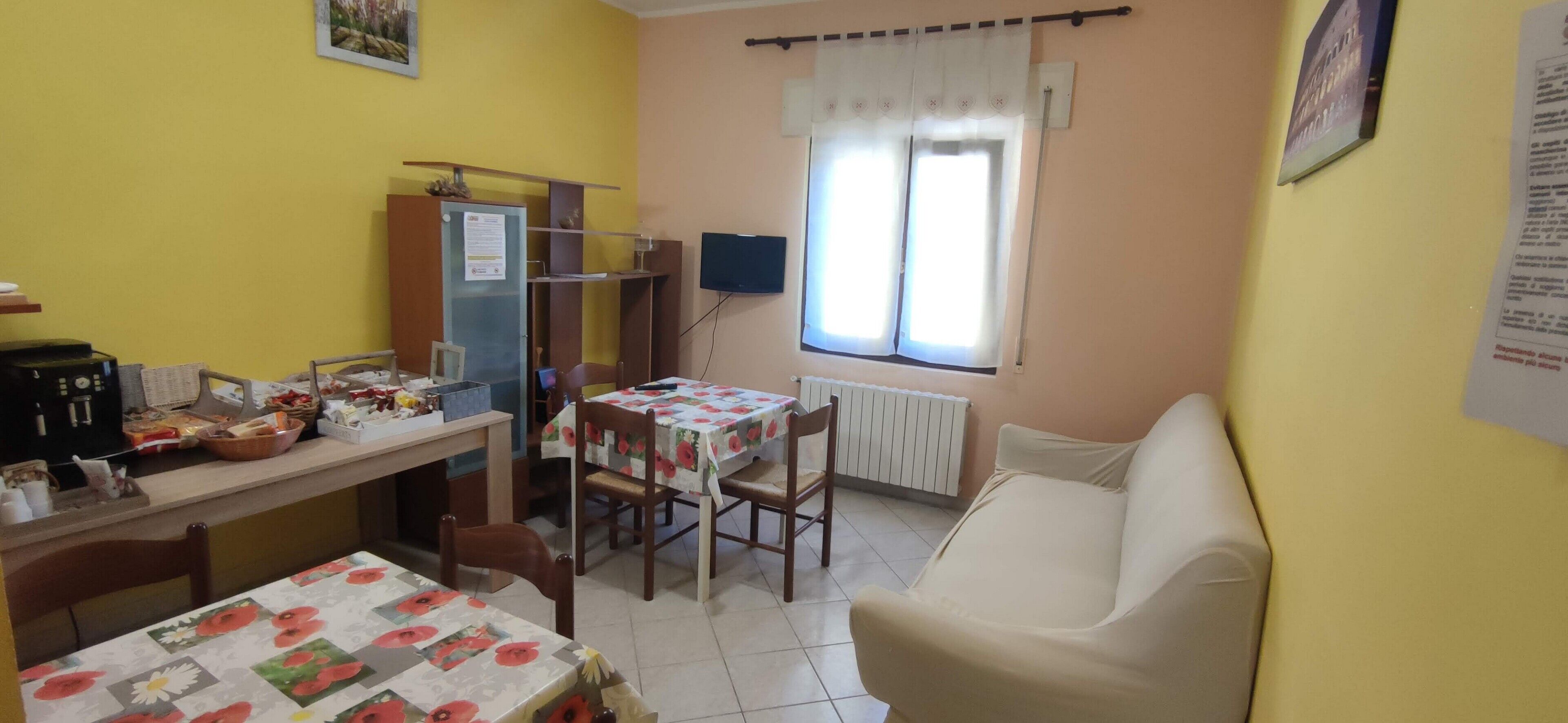 Une cuisine de taille réduite comprenant une table à manger, des chaises, un réfrigérateur et une fenêtre avec des rideaux.