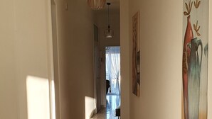 En gang med gulv i høj glans, en pendellampe og et maleri på væggen.