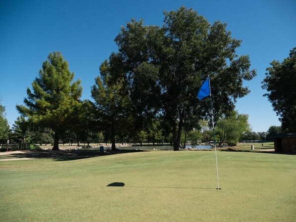 Un campo da golf con una bandiera sul green, alberi e cielo sereno.