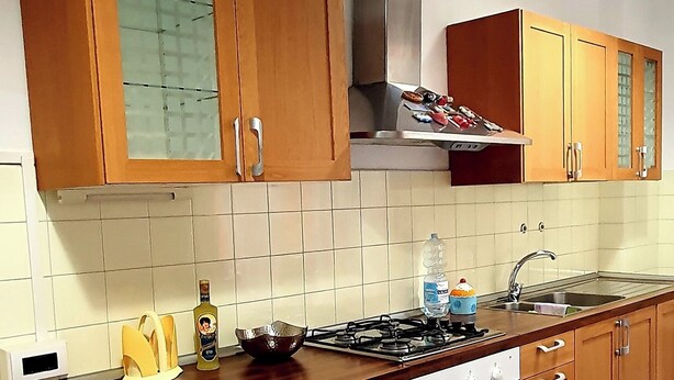 Una cocina con armarios de madera, estufa a gas, campana extractora de acero inoxidable y salpicadero de azulejos.