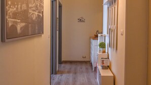 A hallway with wooden flooring, a framed cityscape picture, a hanging light fixture, and a small cabinet with decorative items. - Very cozy apartment on the 3rd floor(with elevator) in downtown Cuneo (Cuneo)