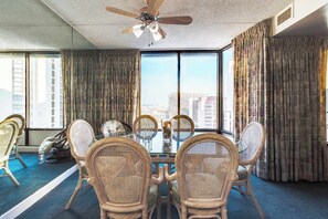 A hotel room with a large window, a ceiling fan, and a dining area with wicker chairs and a glass table.
