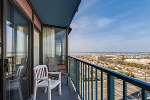 A balcony with a view of the city and ocean. There are two white chairs and a table.