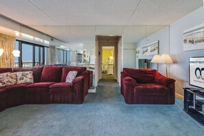 A modern hotel room with a large window, a red sofa, a smaller red sofa, and a TV on a stand.