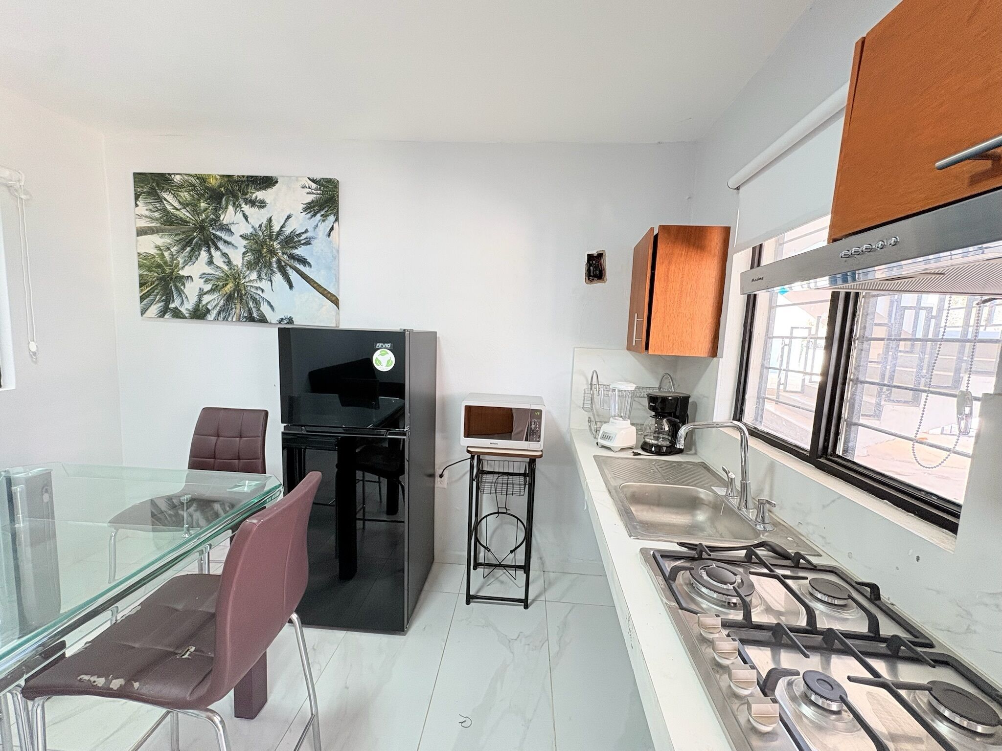 Una cocina compacta con estufa a gas, refrigerador, microondas y licuadora.