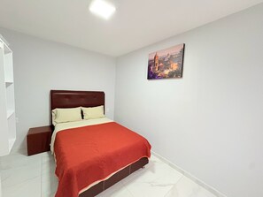 A bedroom with a bed, a nightstand, a painting on the wall, and a white ceiling light. - Residencia Gran Coyula Orange 506 (Tonala)