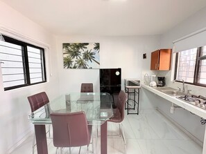 A modern kitchen with a glass dining table, chairs, a refrigerator, a microwave, and a sink.
