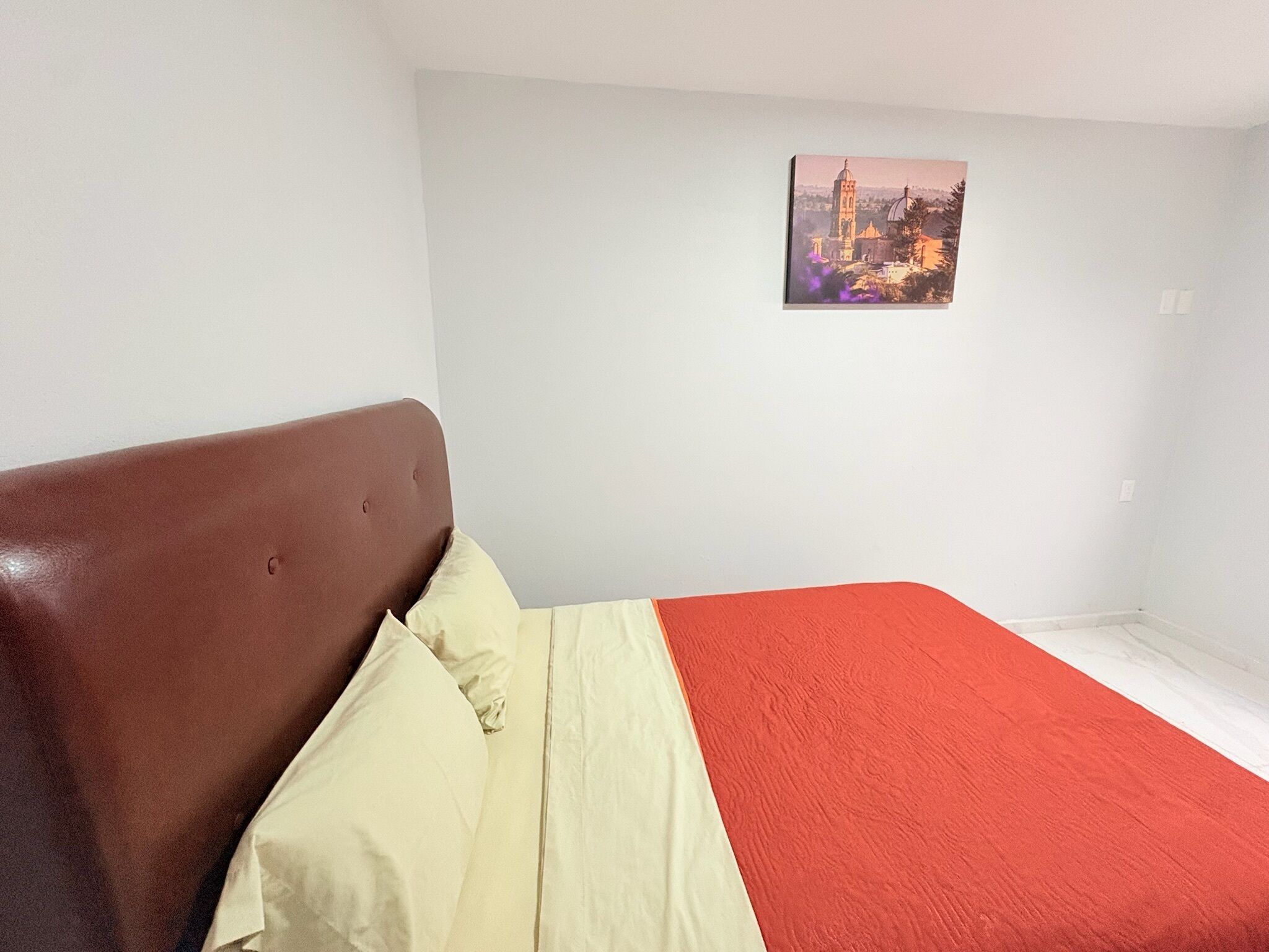 A bedroom with a bed, a headboard, and a wall-mounted picture.