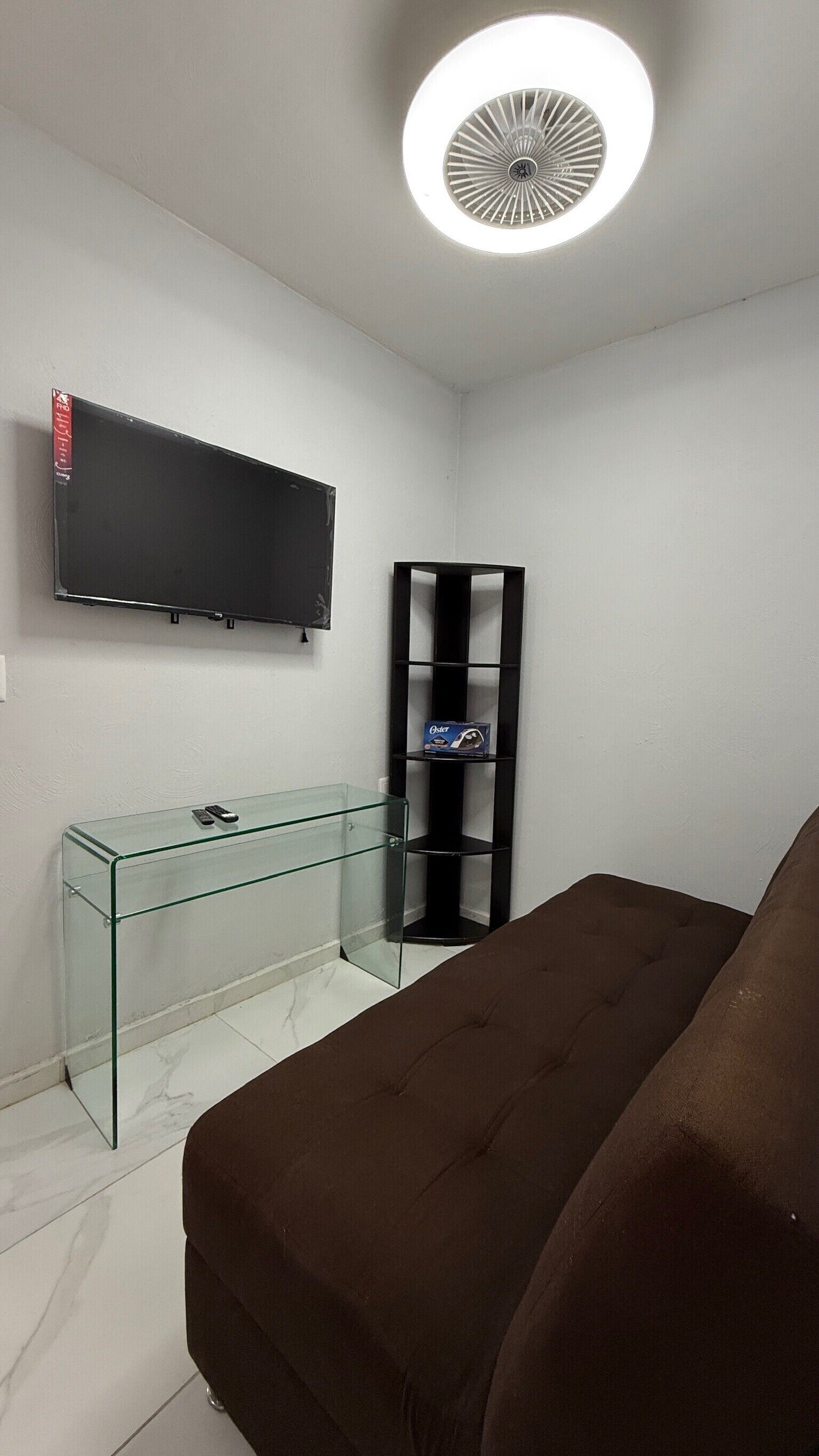 A bedroom with a bed, a glass TV stand, a black shelving unit, and a ceiling light fixture.