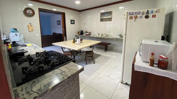 A modern kitchen with a gas stove, a dining table, and a refrigerator. - Maria Antônia's Family Home (Paraty)
