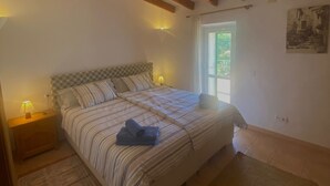 Quarto com cama grande, vigas de madeira no teto, janela e um quadro na parede.